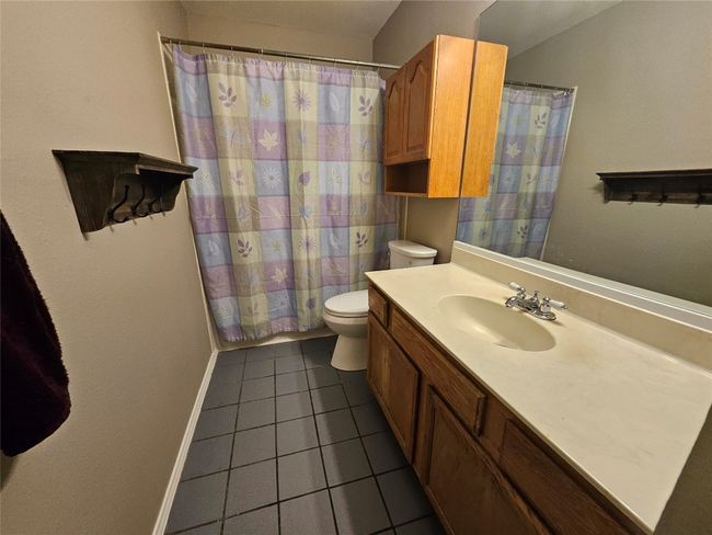 Full bathroom with toilet, a shower with curtain, tile patterned floors, baseboards, and vanity | Image 17