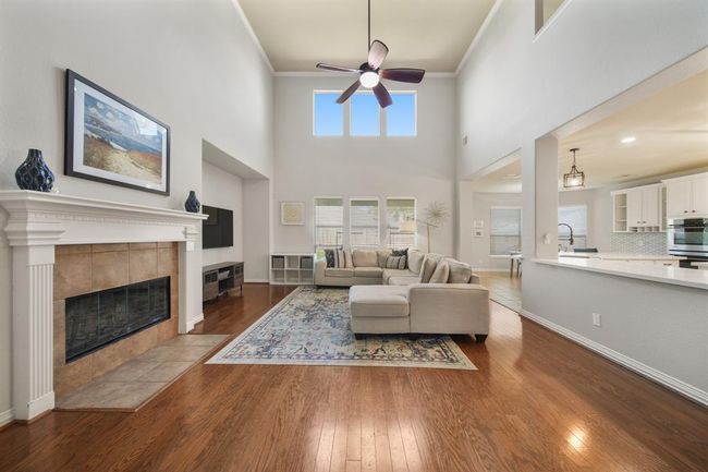 Located on the back of the home, the living room with a soaring two story ceiling features crown moulding, a ceiling fan with lighting, hardwoods, windows with blinds and upper fixed glass windows overlooking the backyard. | Image 10