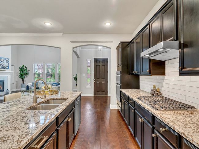 Kitchen with extractor fan, stainless steel appliances, light stone counters, backsplash, and dark wood finished floors | Image 11
