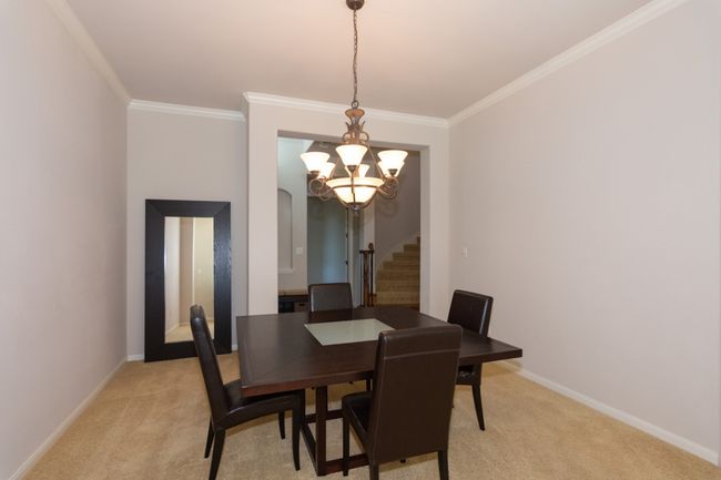Dining area featuring baseboards, a notable chandelier, ornamental molding, stairs, and light carpet | Image 7