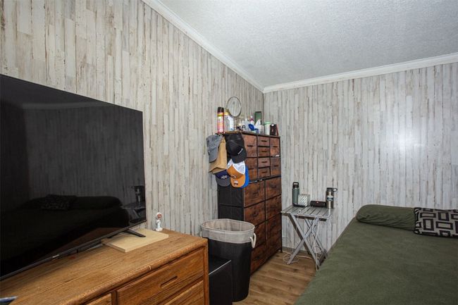 Bedroom featuring a textured ceiling, light wood-type flooring, crown molding, and wooden walls | Image 14