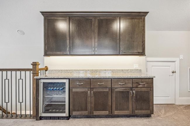 The third-floor bar/ kitchenette area with dark wood cabinetry, a granite countertop, and a built-in fridge. It's perfect for entertaining and adds a convenient option for guests. | Image 24
