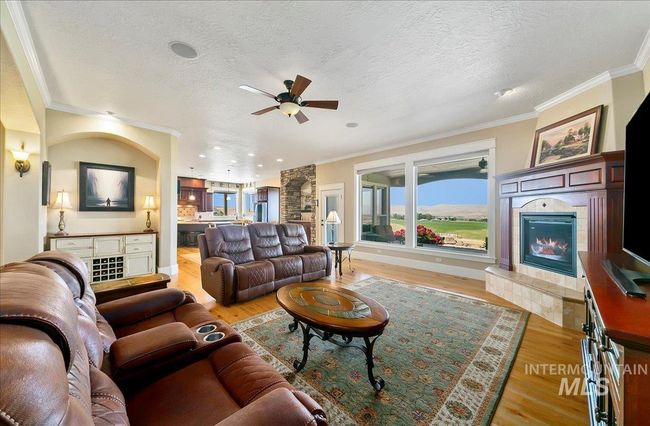 Living room featuring a tile fireplace, light wood-style floors, ceiling fan, crown molding, and a textured ceiling | Image 6