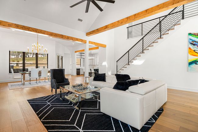 Living room with ceiling fan with notable chandelier, high vaulted ceiling, stairway, and light wood-type flooring | Image 6