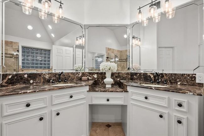 The primary bathroom continues the luxury with dual vanities, custom granite counters, a full wall of mirrors, and sparkling lighting for that spa-like glow. | Image 25