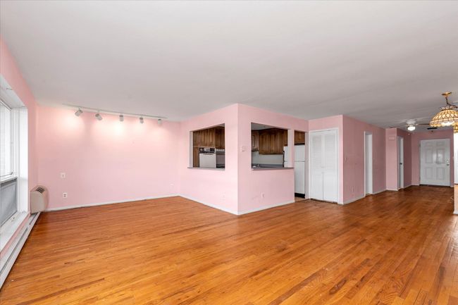 Unfurnished living room with a baseboard heating unit, a wall mounted AC, wood finished floors, and baseboards | Image 10