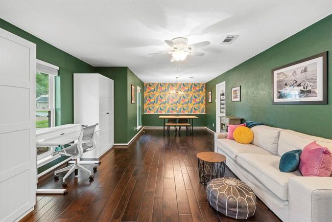 This vibrant formal living and formal dining space features rich hardwood floors and deep green walls. Large windows offer ample natural light, creating a warm and inviting atmosphere. | Image 6