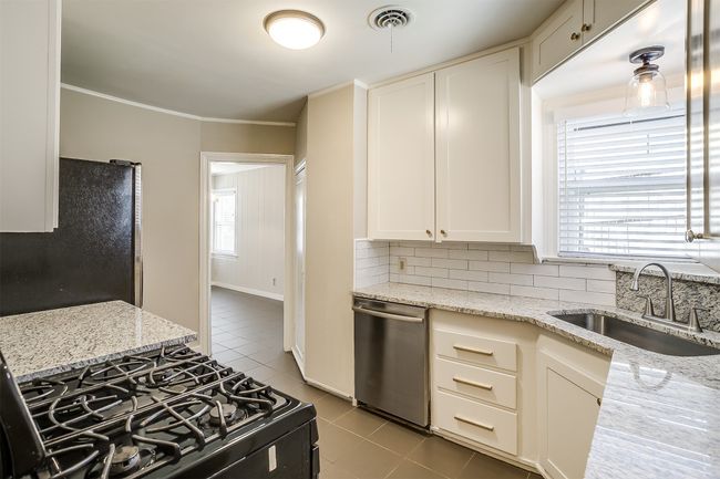 Kitchen with dishwasher, black range with gas stovetop, freestanding refrigerator, light tile patterned flooring, and tasteful backsplash | Image 10