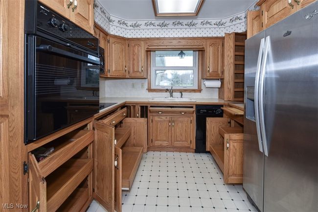 Kitchen with a sink, backsplash, brown cabinets, light countertops, and black appliances | Image 25