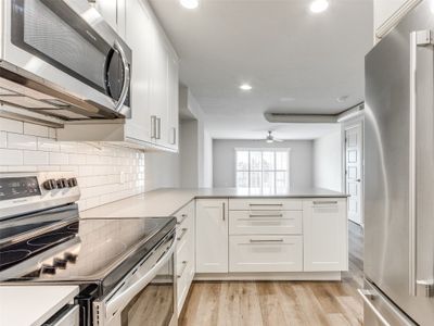 Kitchen with white cabinetry, light hardwood / wood-style flooring, appliances with stainless steel finishes, kitchen peninsula, and tasteful backsplash | Image 1