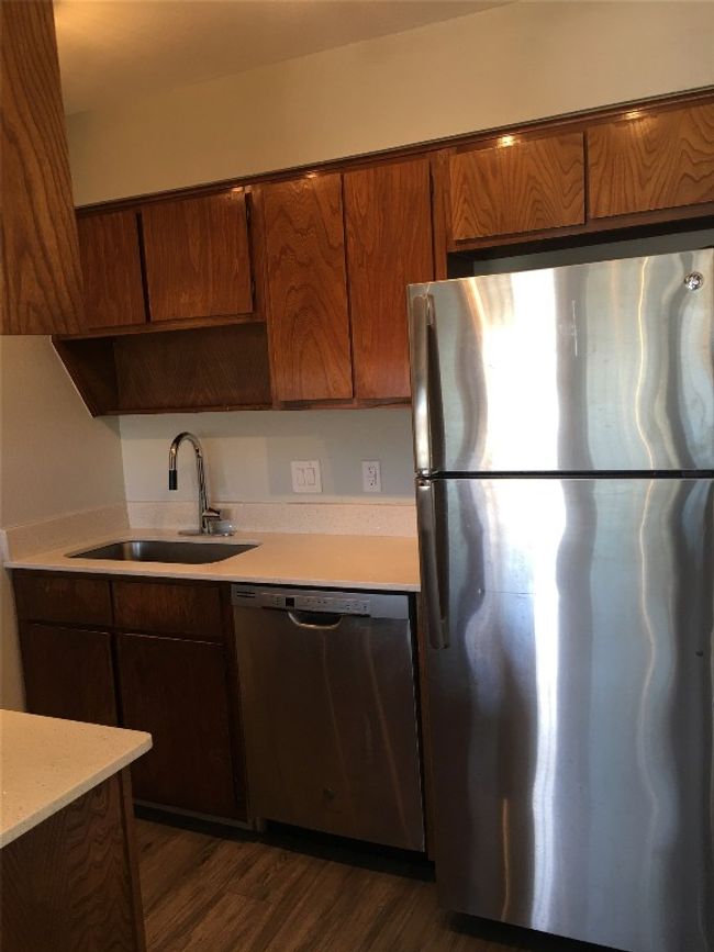 Kitchen with appliances with stainless steel finishes, brown cabinets, a sink, light countertops, and dark wood-type flooring | Image 5
