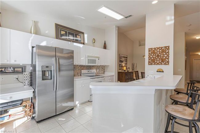 Large kitchen bar/counter, light tile patterned floors, and white cabinetry | Image 4