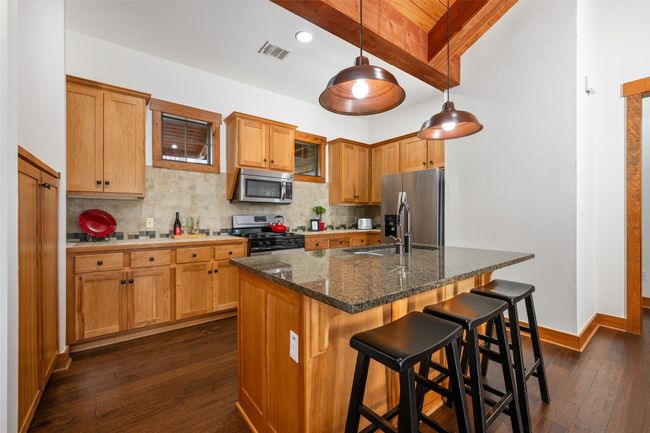 This warm and inviting kitchen features natural wood cabinetry, granite countertops, and stainless steel appliances. A spacious island with bar seating and pendant lighting creates a perfect spot for casual dining or entertaining. The earthy tones and wood finishes blend seamlessly, adding a cozy touch to the heart of the home. | Image 5