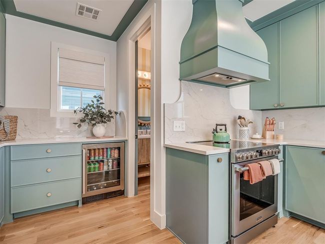 Kitchen with stainless steel range with electric cooktop, custom range hood, beverage cooler, green cabinetry, and tasteful backsplash | Image 15