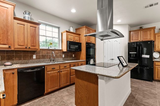 Kitchen featuring island exhaust hood, a center island, backsplash, black appliances, and a sink | Image 12