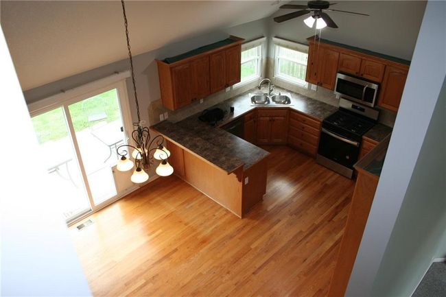 Kitchen featuring a peninsula, vaulted ceiling, stainless steel appliances, dark countertops, and a kitchen bar | Image 6