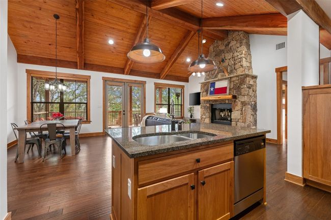 This space connects kitchen, dining, and living areas with vaulted ceilings and a stone fireplace. Large windows offer natural light and views of the surrounding landscape. | Image 6
