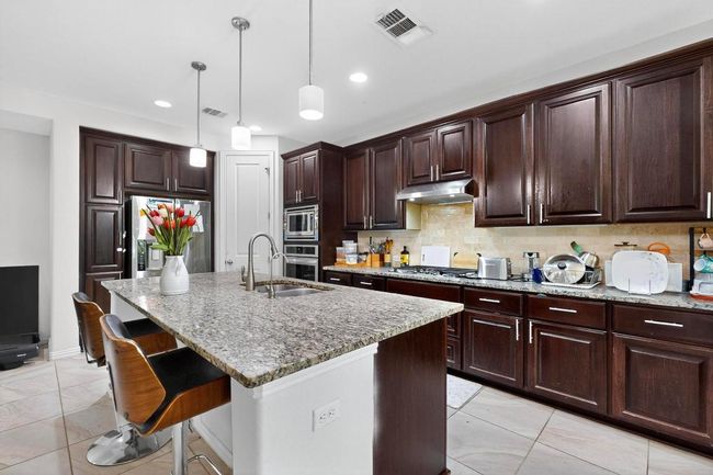 Kitchen featuring stainless steel appliances, exhaust hood, pendant lighting, light stone countertops, and dark brown cabinetry | Image 9