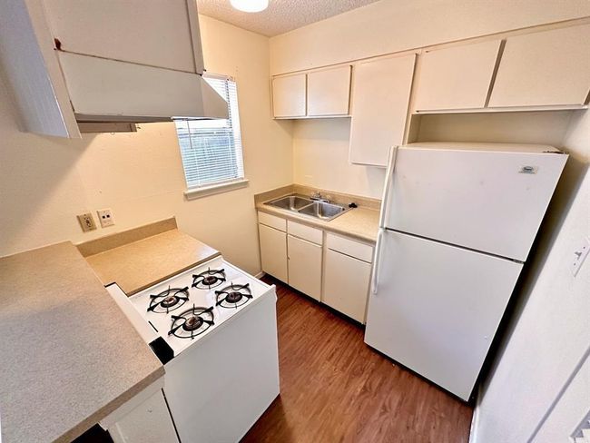 Kitchen featuring white appliances, wood finished floors, light countertops, a sink, and white cabinets | Image 4