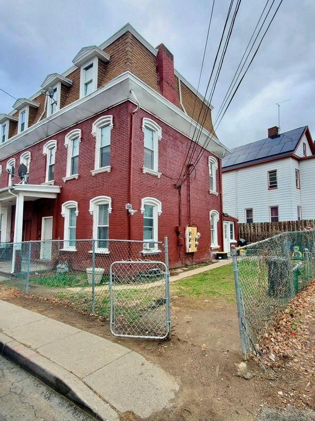 View of property exterior featuring a fenced front yard, mansard roof, and brick siding | Image 4
