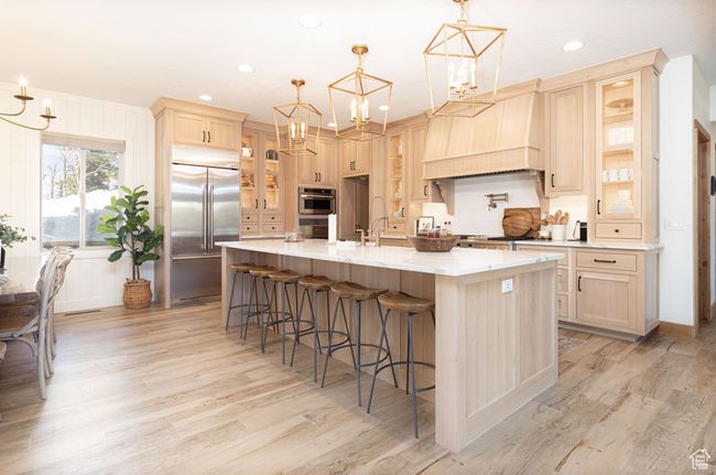 Kitchen featuring light wood finished floors, custom exhaust hood, light brown cabinetry, and appliances with stainless steel finishes | Image 7