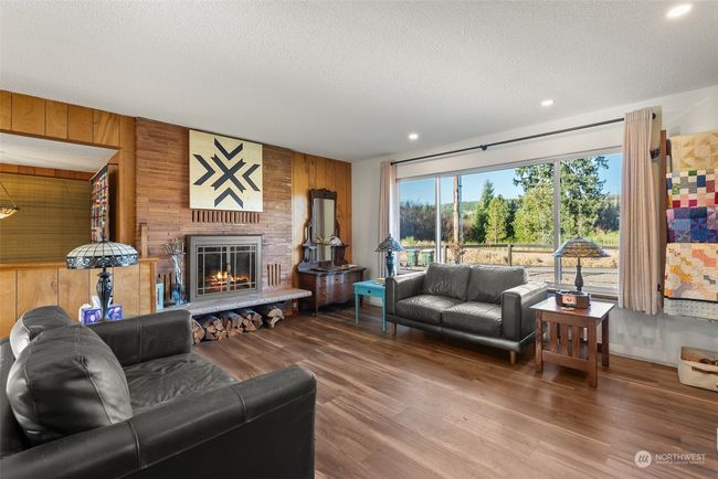 The living room is a bright and inviting space, featuring large new windows that flood the room with natural light. This cheerful setting is ideal for relaxing, entertaining, or simply soaking in the views of the outdoors. On cooler days, enjoy the added warmth and ambiance of the fireplace, making this room the heart of comfort in this home | Image 11