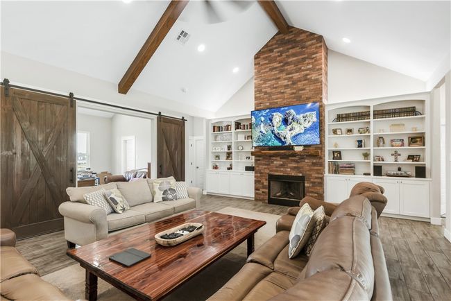 Living area with a barn door, light wood-style flooring, beamed ceiling, high vaulted ceiling, and built in features | Image 5