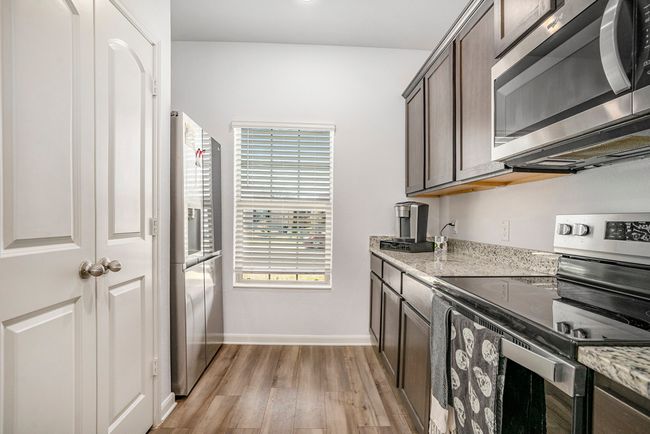 Kitchen featuring light granite counters, appliances with stainless steel finishes, light luxury vinyl plank flooring, baseboards, and dark brown cabinets | Image 9