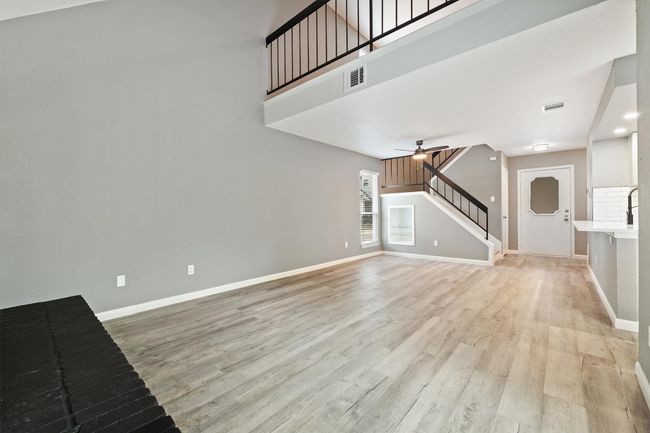 Unfurnished living room featuring a ceiling fan, light wood-style flooring, stairway, baseboards, and a towering ceiling | Image 12