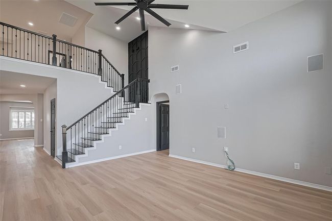 Modern living area features high ceilings with a large ceiling fan, light wood flooring, and an elegant staircase with dark railings. | Image 10