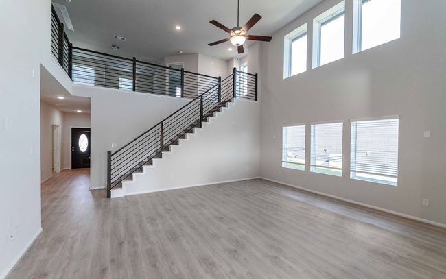 Unfurnished living room with a high ceiling, ceiling fan, stairway, light wood finished floors, and recessed lighting | Image 5