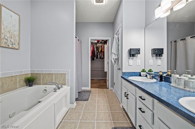 Bathroom with vanity with extensive cabinet space, a washtub, tile flooring, double sink, and a textured ceiling | Image 22