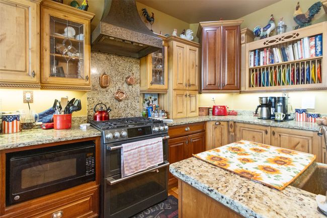 Kitchen with stainless steel range with gas cooktop, custom range hood, black microwave, light stone counters, and decorative backsplash | Image 14
