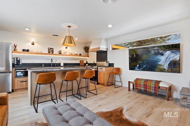 Kitchen featuring custom exhaust hood, appliances with stainless steel finishes, open shelves, dark countertops, and a kitchen breakfast bar | Image 32