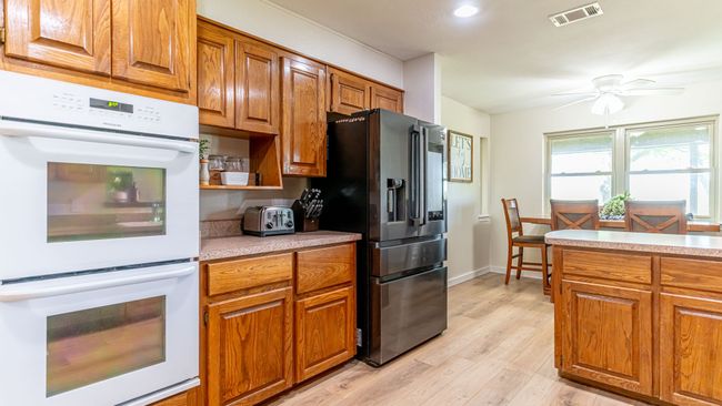 Kitchen with fridge with ice dispenser, double oven, brown cabinets, and visible vents | Image 14