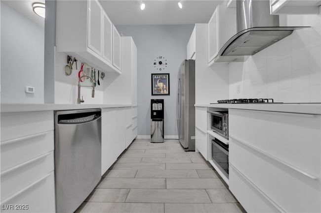 Kitchen with appliances with stainless steel finishes, wall chimney exhaust hood, light countertops, and white cabinets | Image 17