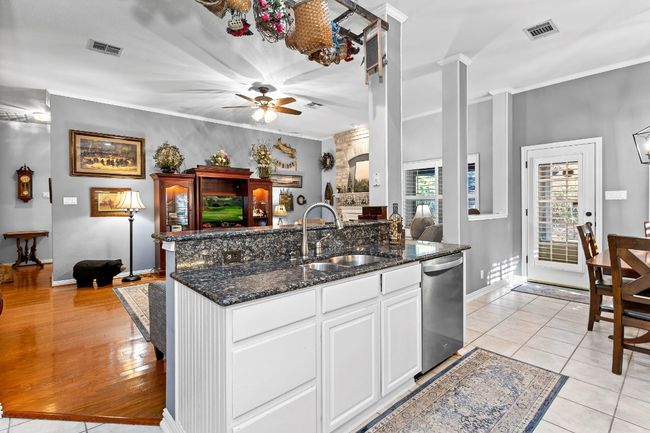 Kitchen with sink, white cabinets, light tile patterned flooring, stainless steel dishwasher, and dark stone counters | Image 13