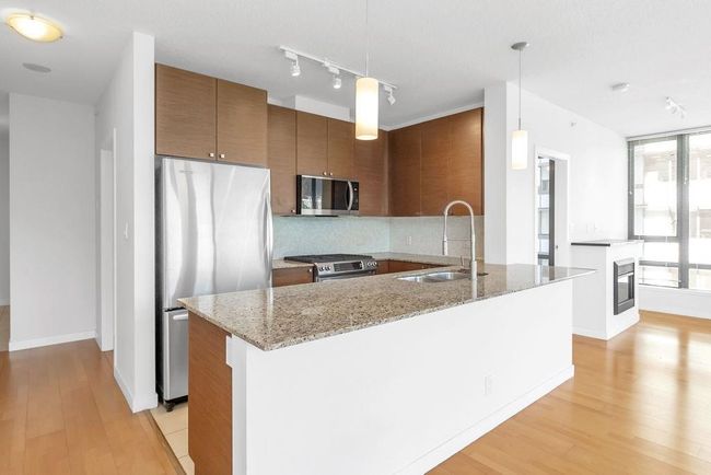 Kitchen with appliances with stainless steel finishes, brown cabinetry, light wood-type flooring, light stone countertops, and decorative backsplash | Image 6