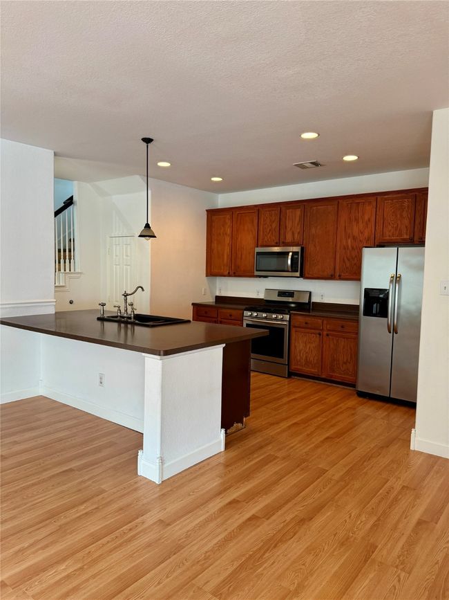 Kitchen featuring appliances with stainless steel finishes, dark countertops, a sink, light wood-type flooring, and pendant lighting | Image 10