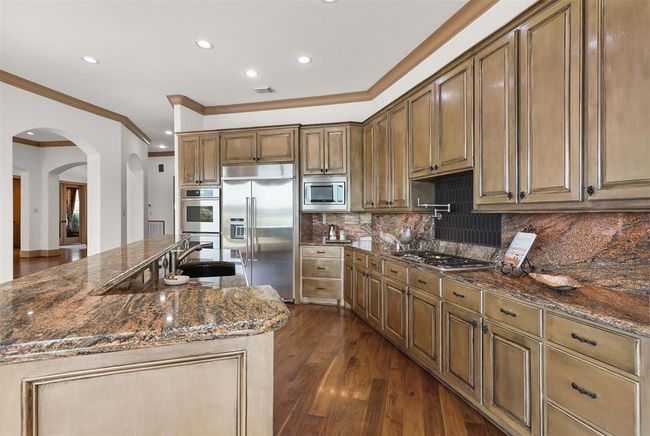 This spacious kitchen features elegant wooden cabinetry, granite countertops, stainless steel appliances, and a large island with a breakfast bar, perfect for cooking and entertaining. | Image 22