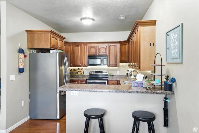 Kitchen with appliances with stainless steel finishes, a peninsula, dark wood-style flooring, a breakfast bar area, and a textured ceiling | Image 11