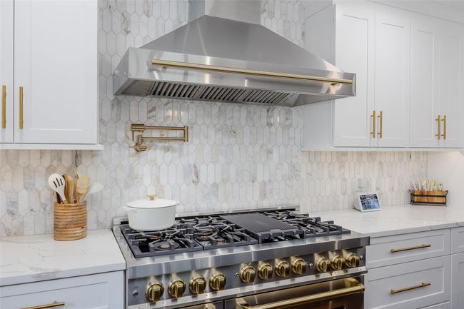 Kitchen with wall chimney range hood, stainless steel range, decorative backsplash, white cabinets, and light stone counters | Image 7