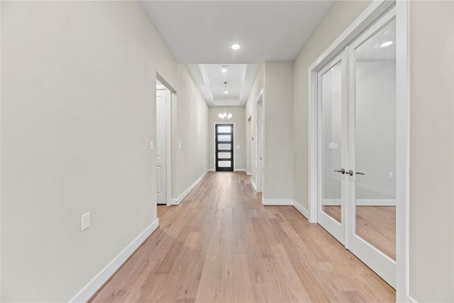 The foyer sets a stylish tone with a raised tray ceiling, chic chandelier, and warm luxury vinyl plank flooring that flows throughout the home. French doors to the right open into a spacious private study, perfect for work, hobbies, or a quiet retreat. | Image 5