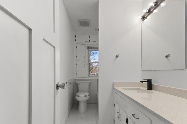 Main level Full bathroom features a quartz countertop, custom storage cabinetry, ceramic tile tub surround, wainscoting and floors | Image 20