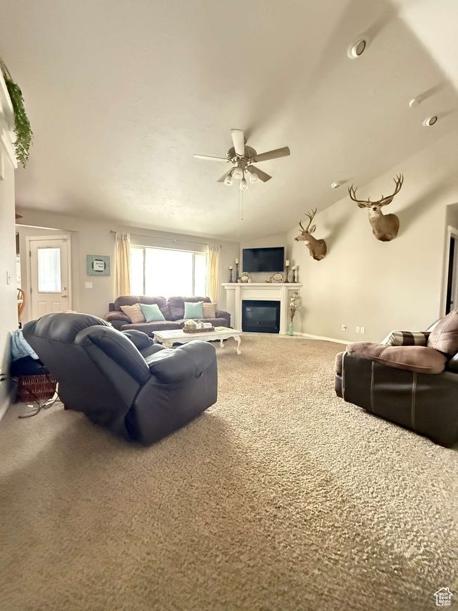 Living area with carpet flooring, ceiling fan, a glass covered fireplace, and baseboards | Image 10