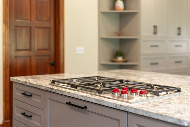 Kitchen with stainless steel gas stovetop, light stone countertops, open shelves, and gray cabinets | Image 9