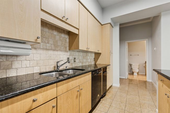 Kitchen with decorative backsplash, dark stone counters, black dishwasher, and light brown cabinets | Image 13