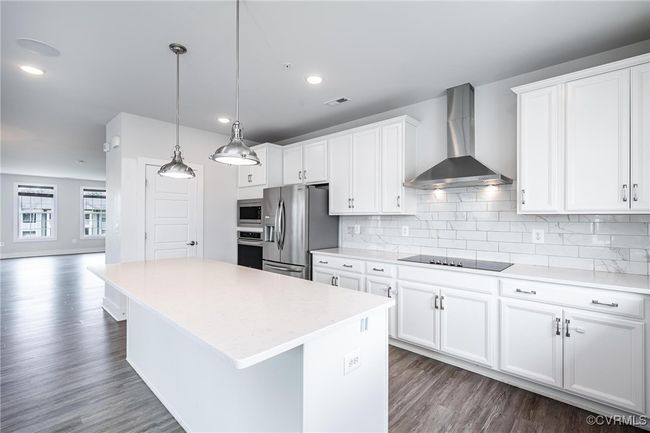 Kitchen featuring wall chimney exhaust hood, appliances with stainless steel finishes, a kitchen island, light countertops, and dark wood-style floors | Image 9