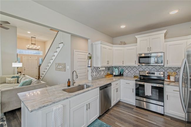 Kitchen featuring appliances with stainless steel finishes, a peninsula, white cabinets, dark wood-style floors, and open floor plan | Image 12