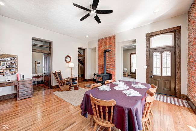 dining area featuring a wood stove, ceiling fan, brick wall, light wood finished floors, and baseboards | Image 13